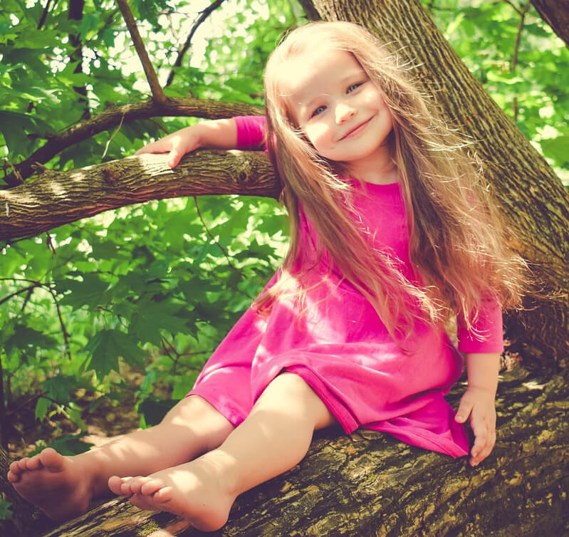 Young girl in pink dress sitting in a tree.